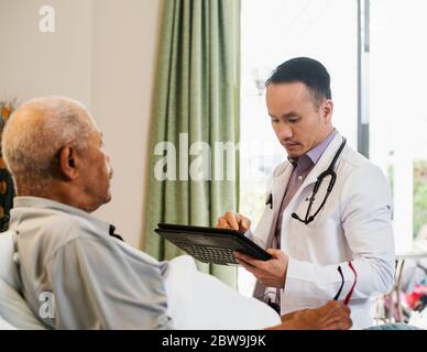 Doctor using tablet while visiting senior man in nursing home Stock Photo