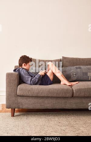 Boy (8-9) using tablet on sofa Stock Photo