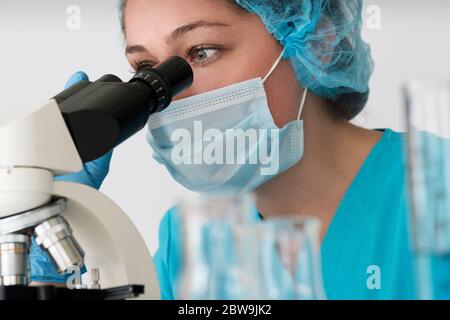 Laboratory technician in face mask looking through microscope Stock Photo