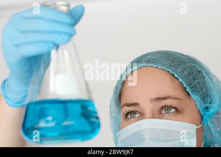 Laboratory technician in face mask holding flask with liquid Stock Photo