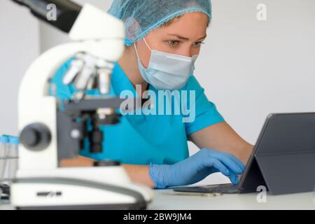 Laboratory technician using tablet next to microscope Stock Photo