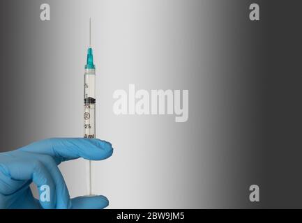 Close-up of hand in blue surgical glove holding syringe Stock Photo
