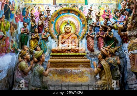 A seated Buddha statue surrounded by worshippers  inside the Angurukaramulla Temple at Negombo in Sri Lanka. The temple is over 300 years old. Stock Photo