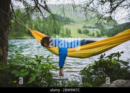 Switzerland, Bravuogn, Palpuognasee, Young woman resting in hammock near Palpuognasee lake in Swiss Alps Stock Photo