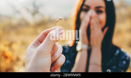 Close up photo of a wedding ring with diamond shown to the girl while she is amazed and covers her face with palms Stock Photo