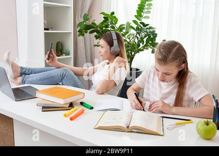 Mother is not helping daughter to do homework while using her smart phone and listening to music with headphones  Stock Photo
