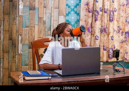 young black woman sitting at home, vlogging with her smartphone while working on her laptop Stock Photo