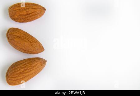 Nuts Almond kernels three pieces close-up lie on a white background on the left side.copyspace for text Stock Photo