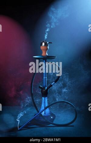 Smoking a hookah on a dark blue background, with smoke and neon light Stock Photo