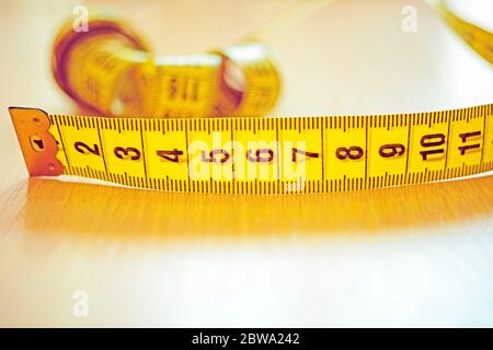 Yellow measuring tape with black scale on the wooden table. Stock Photo