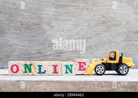 Toy bulldozer hold letter block e to complete word online on wood background Stock Photo