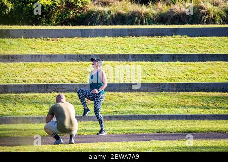 Woman exercising in lycra in park with personal trainer watching on,Sydney,Australia early morning exercise Stock Photo