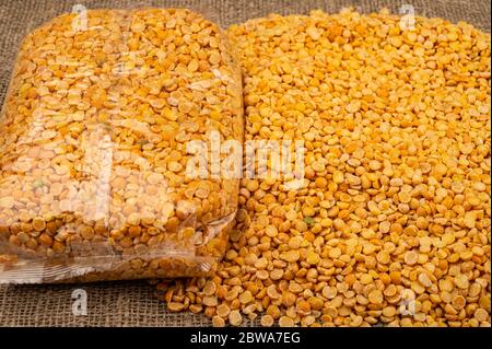Yellow split peas in a plastic bag and cereal in bulk on a background of burlap with a rough texture. Traditional cereals for making soups and porridg Stock Photo