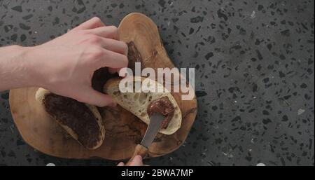 man spreading chocolate spread on ciabatta slice on olive board top view Stock Photo