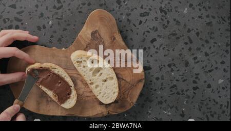 man spreading chocolate spread on ciabatta slice on olive board top view Stock Photo
