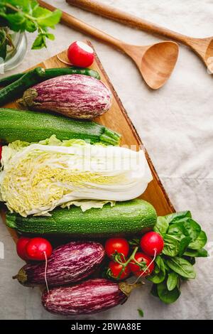 Different vibrant fresh vegetables on a table with wooden kitchen utensils. Stock Photo