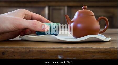 Chinese red clay pot and small cup on handmade ceramic leave shaped plate on wooden table Stock Photo