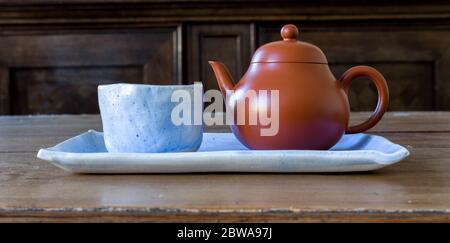 Small Light Blue Ceramic Handmade Tea Cup with small brown teapot on light blue ceramic plate and wooden table. True Chinese tea culture for green tea Stock Photo