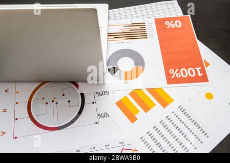 Laptop and papers with graphics and statistics on a dark wooden table Stock Photo