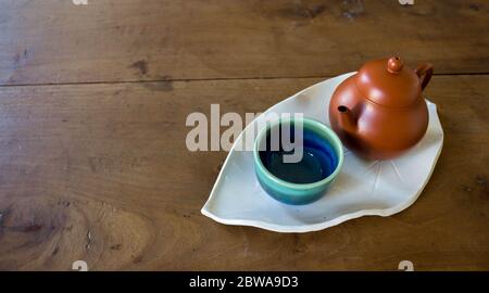 Chinese red clay pot and small cup on handmade ceramic leave shaped plate on wooden table Stock Photo