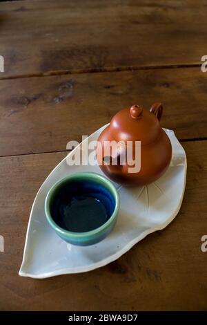 Chinese red clay pot and small cup on handmade ceramic leave shaped plate on wooden table Stock Photo