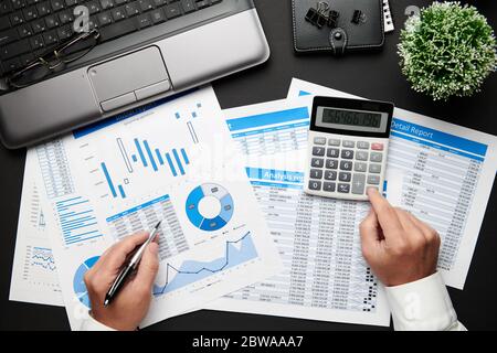 Top view of businessman's hands working with financial reports. Modern black office desk with laptop, notebook, pencil and a lot of things. Flat lay t Stock Photo