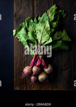 Bunch of fresh beetroots on wooden board ready for chopping, black background, top view Stock Photo