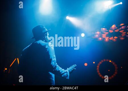 Dark-skinned singer in a suit and hat on a stage illuminated  Stock Photo