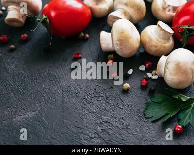 Food ingredients on black background, copy space Mini champignons, cherry tomatoes, herbs and spices top view or flat lay Stock Photo