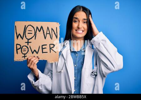 Young doctor woman wearing stethoscope holding cardboard banner with powe message stressed with hand on head, shocked with shame and surprise face, an Stock Photo