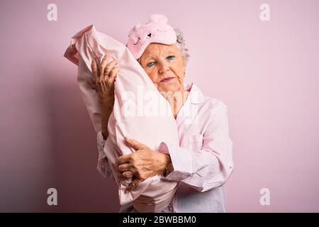 Senior beautiful woman wearing sleep mask holding pillow over isolated pink background with a confident expression on smart face thinking serious Stock Photo