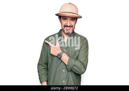Middle age tourist man on vacation wearing explorer hat over isolated white background smiling cheerful pointing with hand and finger up to the side Stock Photo