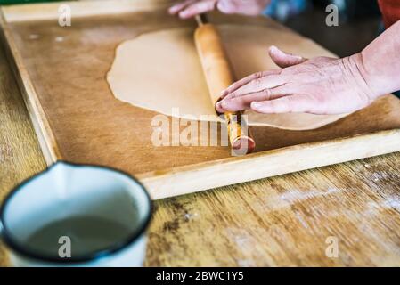 Close up of woman preparing home made fresh pasta the traditional way at home. Rolling pasta dough with rolling pin Stock Photo