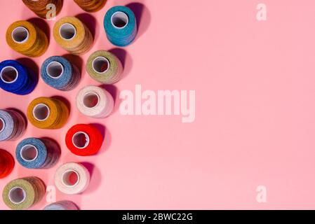 Sewing flat lay with copy space. Top view of sewing supplies, multicolored sewing threads, on pink background. Dressmaking industry and handcraft Stock Photo