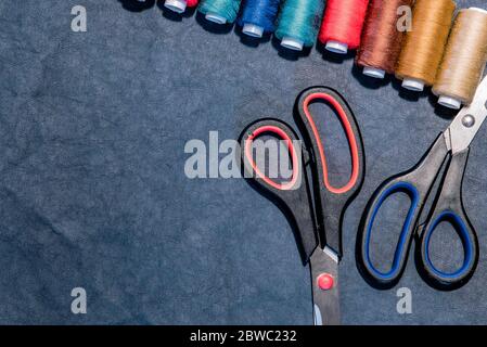 Sewing flat lay with copy space. Top view of sewing accessories on dark background: sewing threads and scissors. Dressmaking industry and handcraft Stock Photo