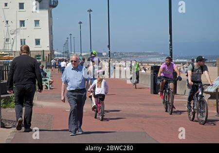 Portobello, Edinburgh, cycling Scotland, UK.  31 May 2020. Sunny but Windy with 14 degrees centigrade,and ENE at 20 km/h and Gusts of 38 km/h, many preferred to stay wrapped up but those lying and sitting on the beach appeared to feel it was warm enough between 12 noon and 1pm. The two Police officers on the promenade might report themselves for not keeping their social disance from each other. One local family and three young boys braved the choppy Firth of Forth for a bit of fun in the sea. Stock Photo