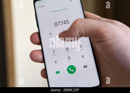 A man's holding an Android smartphone in his hand and typing / dialing a phone number with his thumb, UK Stock Photo