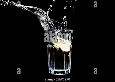 Apple splashing into glass of water on black background. Transparent liquid in motion with droplets. Refreshing fruit beverage with water Stock Photo