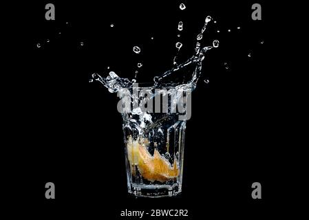 Orange splashing into glass of water on black background. Transparent liquid in motion with droplets. Refreshing fruit beverage with water. Concept of Stock Photo