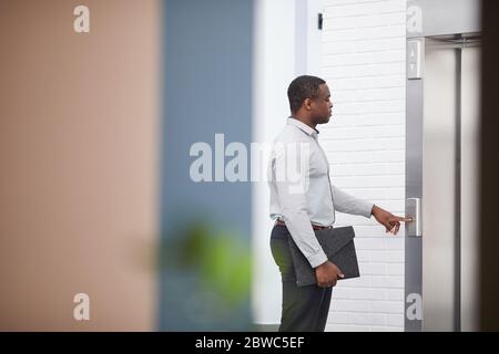 Side view portrait of African-American businessman pushing elevator button in office hall, copy space Stock Photo