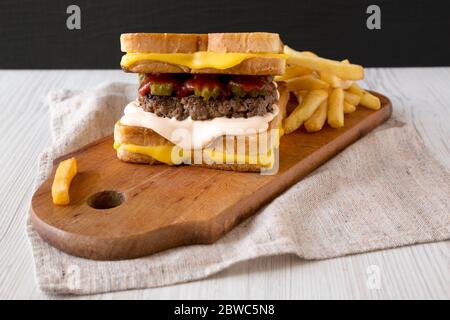 Fresh Grilled Cheese Burger with French Fries on a rustic wooden board, side view. Close-up. Stock Photo