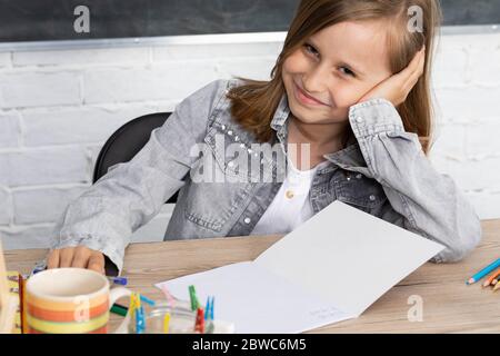 A young schoolgirl is sitting in the classroom. The girl supports her head with her hands. Is smiling. Stock Photo