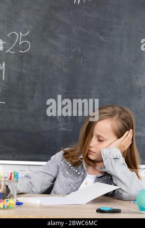 A young schoolgirl is sitting in the classroom. The girl supports her head with her hands. Is smiling. Stock Photo