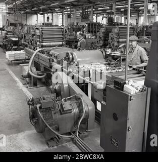 1950s, historical, interior view of the printing presses with male workers in overalls operating the machinery to produce packaging at a battery manufacturing factory, england, UK. Stock Photo