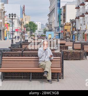 Senior Asian masked man drinks coffee alone on a bench in the city alley Stock Photo