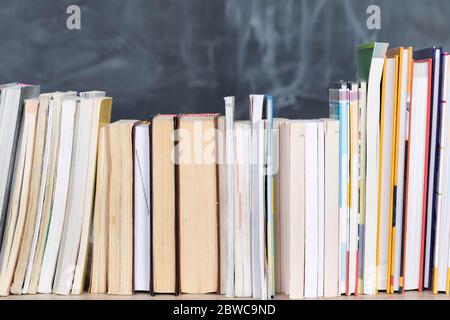 School readings. Stack of many books. A school board in the background is not thoroughly wiped with a sponge. Traces of chalk on the chalkboard. Stock Photo