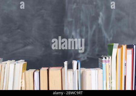School readings. Stack of many books. A school board in the background is not thoroughly wiped with a sponge. Traces of chalk on the chalkboard. Stock Photo