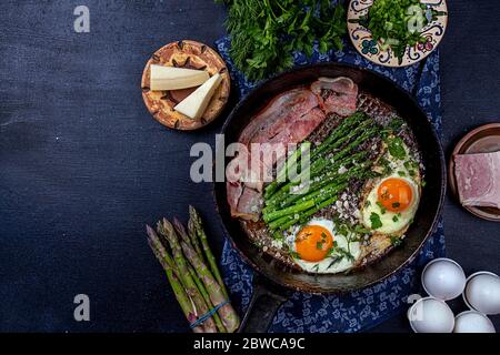 Delicious breakfast lunch branch of fried eggs, bacon, green asparagus, greenery and parmesan cheese on pan. top view, copy space Stock Photo