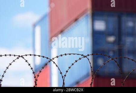 Freight shipping containers stacked up behind barbed wire at a busy European sea port