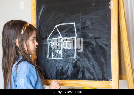 the girl drew a house and the sun with chalk on the Board, so she learns to draw Stock Photo